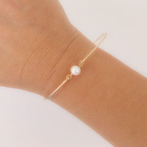 May include: A delicate gold bangle bracelet with a single white pearl accent. The bracelet is simple and elegant, perfect for everyday wear.