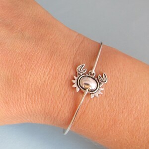 May include: A silver bangle bracelet with a crab charm. The charm is detailed with a textured shell and claws.