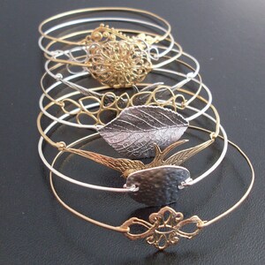 Pode incluir: Um conjunto de seis pulseiras de bracelete de prata e ouro com pingentes decorativos. Os pingentes incluem uma folha, um p&aacute;ssaro, uma flor e um design geom&eacute;trico.