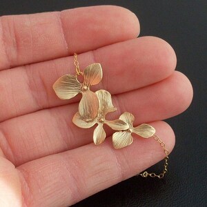 May include: Gold necklace with a delicate chain and three gold flower charms. The flowers are arranged in a cascading design.