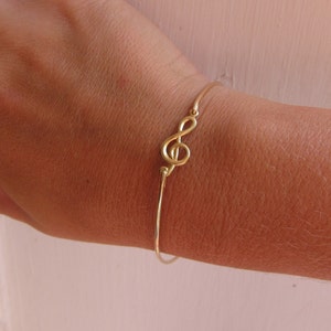 May include: A gold-toned bracelet with a treble clef charm. The bracelet is adjustable and has a simple design.