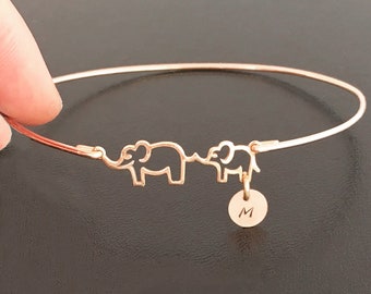 May include: A rose gold bangle bracelet with two elephant charms and a small charm with the letter "M" engraved on it.