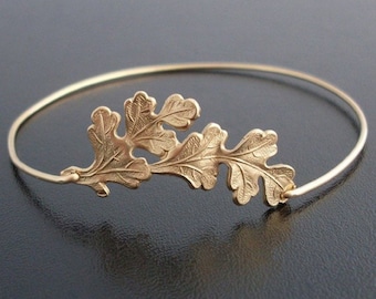 May include: A gold-toned bangle bracelet with a delicate oak leaf design. The leaves are textured and have a slightly raised appearance.