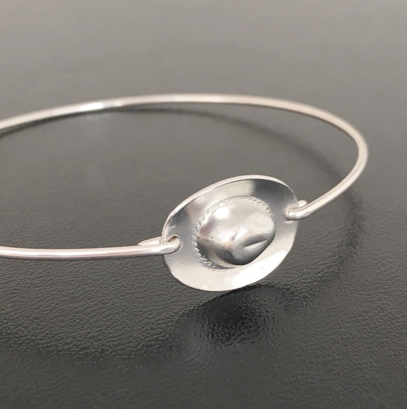 May include: A silver bracelet with a small, round charm in the shape of a cowboy hat.