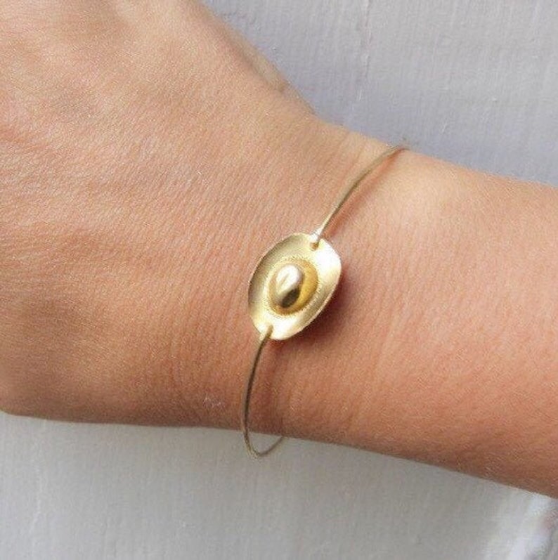 May include: A gold bracelet with a small, round, gold charm in the shape of a hat.