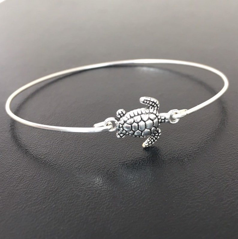May include: A silver bangle bracelet with a turtle charm. The turtle is detailed with a textured shell and is facing to the right.