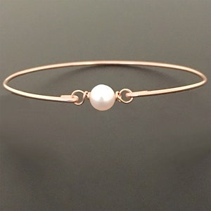 May include: A delicate rose gold bangle bracelet with a single white pearl charm.
