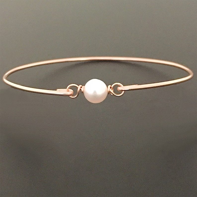 May include: A delicate rose gold bangle bracelet with a single white pearl charm.