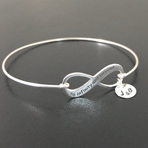 May include: Silver infinity bangle bracelet with the inscription "to infinity and beyond" and a charm with the initials "J & B".