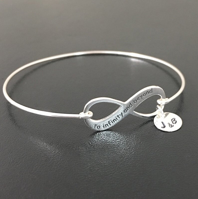 May include: Silver infinity bangle bracelet with the inscription "to infinity and beyond" and a charm with the initials "J & B".