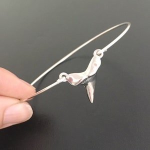 May include: A silver bracelet with a shark tooth charm. The bracelet is made of thin wire and has a simple design.