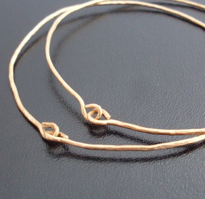 May include: Two gold-toned bangle bracelets with hammered textures and simple, looped closures.