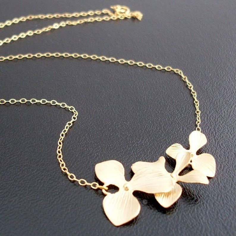 May include: A gold necklace with a delicate chain and a pendant featuring three stylized gold leaves.