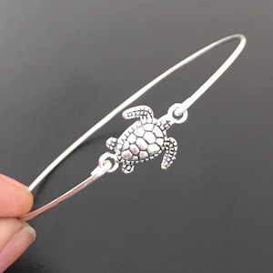 May include: A silver bangle bracelet with a silver turtle charm. The bracelet is open and adjustable.