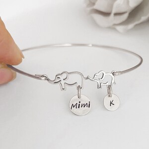 May include: Silver bangle bracelet with two elephant charms and two round charms. One charm is engraved with "Mimi" and the other with the letter "K".