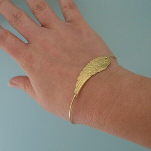 May include: A gold-toned bracelet with a wing-shaped charm. The bracelet is adjustable and has a simple design.