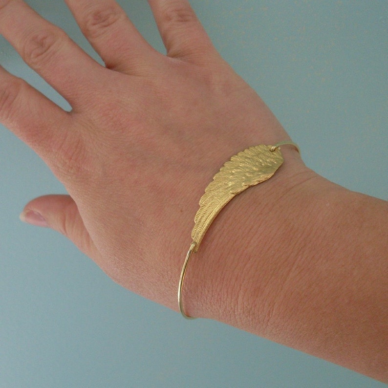 May include: A gold-toned bracelet with a wing-shaped charm. The bracelet is adjustable and has a simple design.