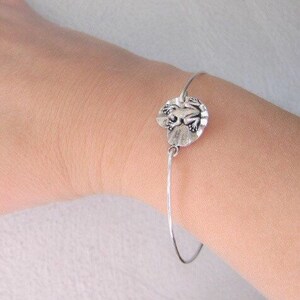 May include: A silver bracelet with a frog charm. The charm is round and features a detailed frog design.