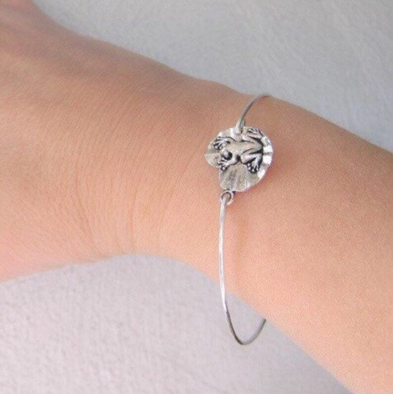 May include: A silver bracelet with a frog charm. The charm is round and features a detailed frog design.