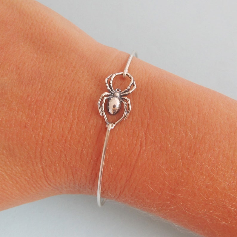 Pode incluir: Um bracelete de prata com um fecho de aranha. A aranha &eacute; detalhada e tem oito patas.