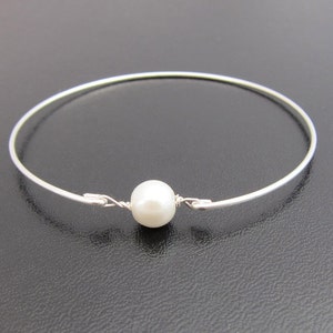 May include: A simple silver bangle bracelet with a single white pearl accent.