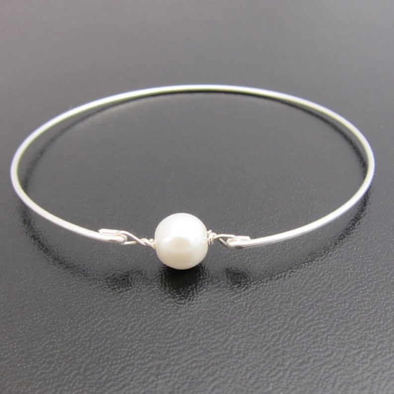 May include: A simple silver bangle bracelet with a single white pearl accent.