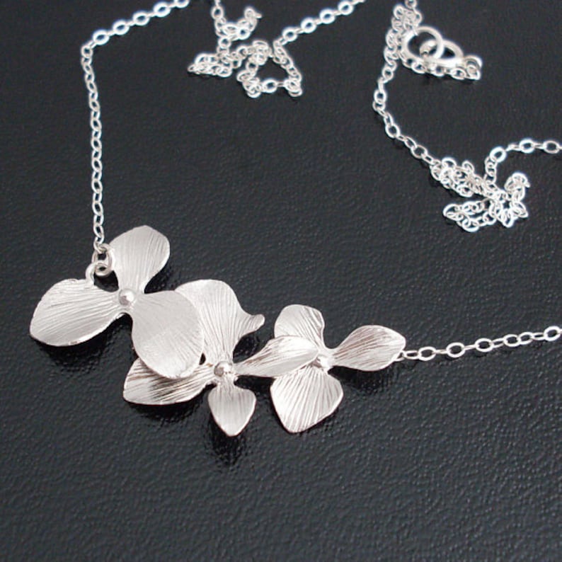 May include: A silver necklace with a delicate chain and a pendant featuring three stylized orchid flowers.