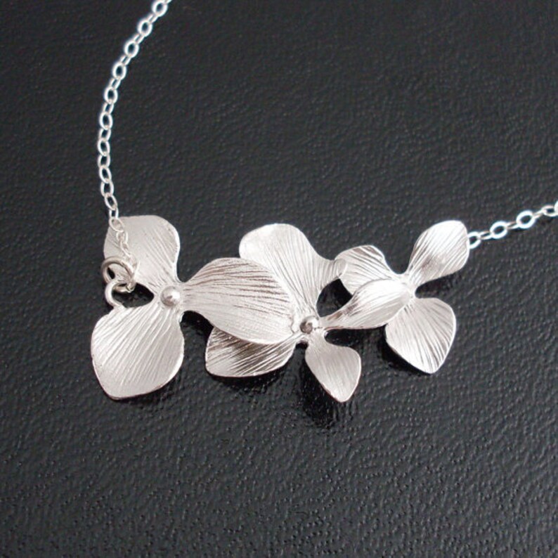 May include: A silver necklace with a pendant featuring three orchid flowers.