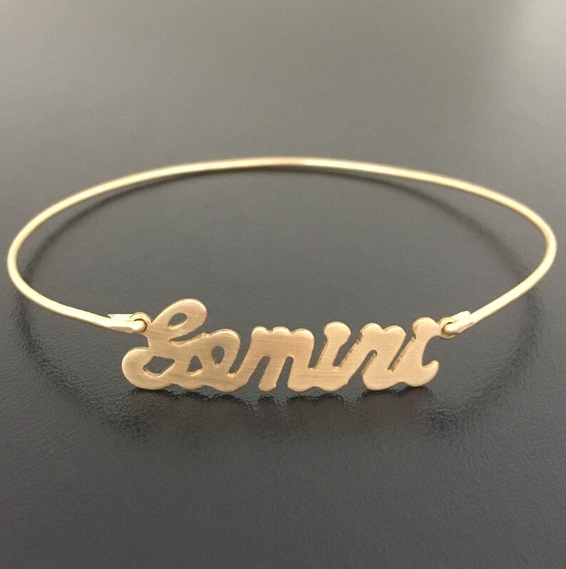 May include: A gold-toned bangle bracelet with the name "Samira" written in a cursive font.