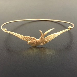 Pu&ograve; includere: Un braccialetto rigido color oro con un design dettagliato di un uccello in volo. Le ali dell'uccello sono spiegate e il braccialetto ha un design semplice ed elegante. Il gioiello &egrave; probabilmente in metallo.