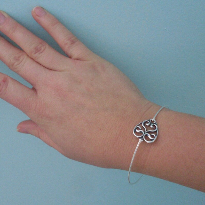 Puede incluir: Una pulsera de plata con un delicado encanto adornado en forma de coraz&oacute;n. El encanto presenta un dise&ntilde;o en espiral e intrincado.