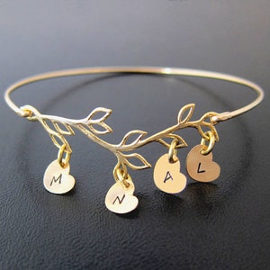 May include: Gold bangle bracelet with a delicate branch design and dangling heart charms. Each heart charm is engraved with a letter, spelling out the name "MALN".