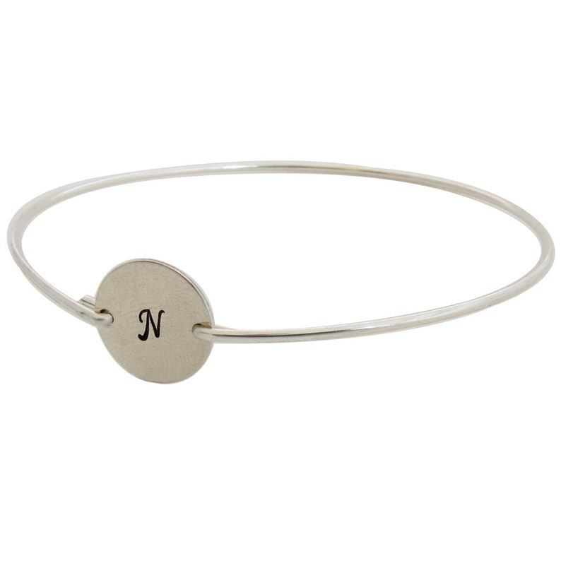 May include: A silver bangle bracelet with a round charm that has the letter "N" engraved on it.