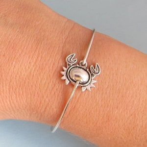 May include: A silver bangle bracelet with a crab charm. The crab is detailed with claws, eyes, and a shell.