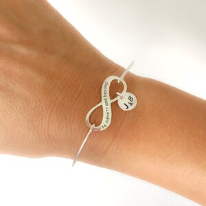 May include: Silver infinity bangle bracelet with the inscription "to infinity and beyond" and a charm with the initials "J & B".