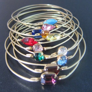 May include: A set of ten gold-toned bangle bracelets with colorful rhinestone accents. The rhinestones are in various shapes and sizes, including teardrop, round, and square.