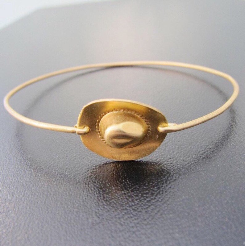 May include: A gold-toned bracelet with a small, round charm in the shape of a cowboy hat.