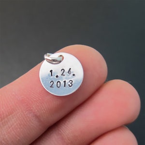 May include: Silver charm with a round disc featuring the date "1.24. 2013" engraved on it.