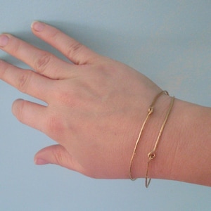 May include: Two gold bracelets with a knotted design. The bracelets are worn on a person's wrist.