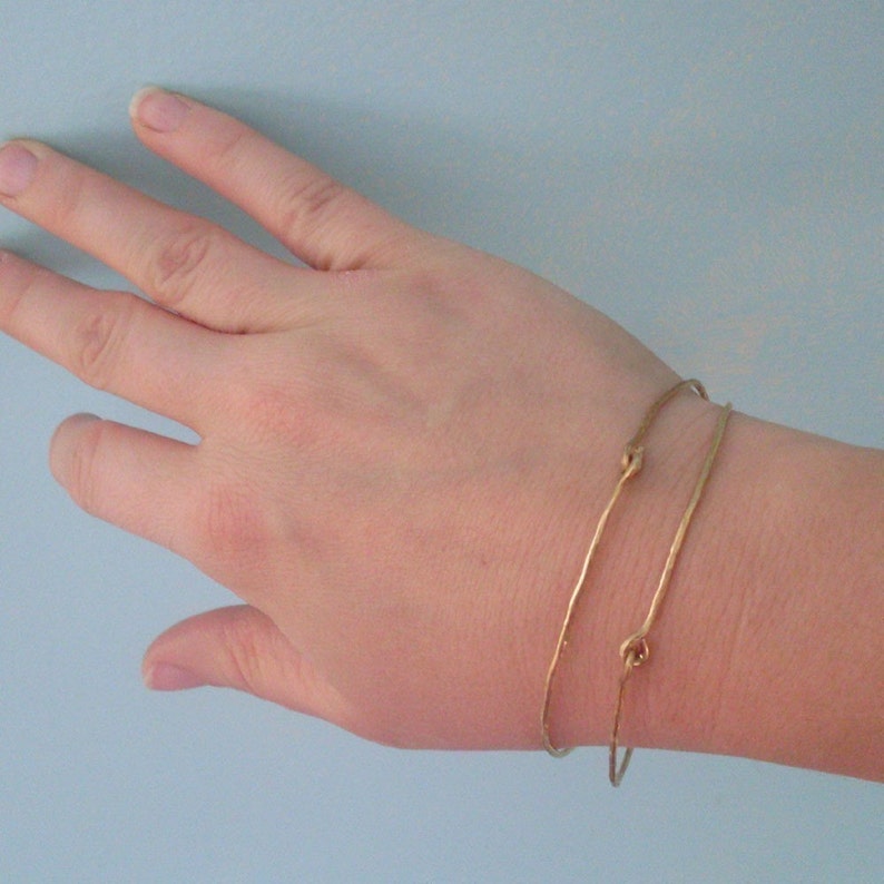 May include: Two gold bracelets with a knotted design. The bracelets are worn on a person's wrist.