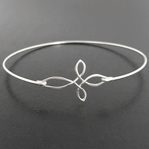 May include: A silver bangle bracelet with a Celtic knot design. The knot is in the shape of a cross.