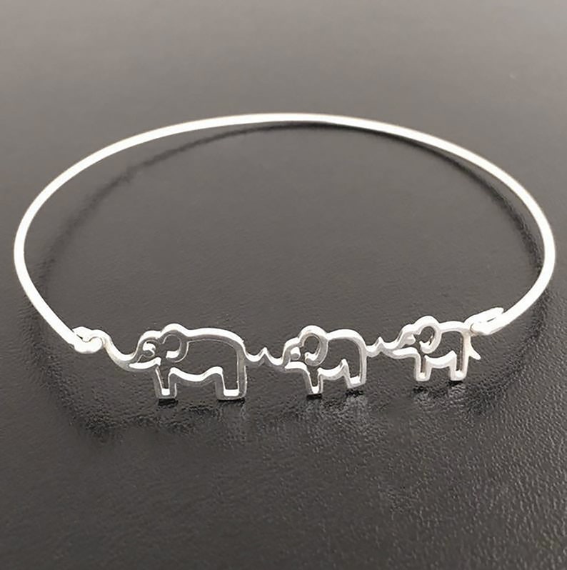 Puede incluir: Pulsera de brazalete de plata con tres siluetas de elefantes. Los elefantes est&aacute;n conectados por una l&iacute;nea fina.