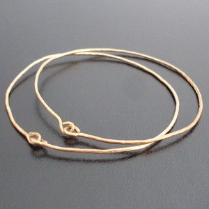 May include: Two gold-toned metal hoops, one slightly larger than the other, are stacked on top of each other. The hoops are smooth and have a slightly hammered texture.