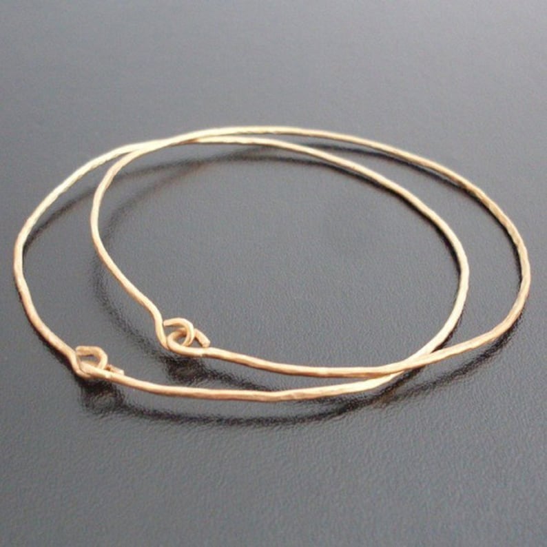 May include: Two gold-toned metal hoops, one slightly larger than the other, are stacked on top of each other. The hoops are smooth and have a slightly hammered texture.