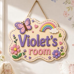 May include: A light-colored wooden wall sign with a scalloped edge, featuring the purple text "Violet's room". The sign is decorated with a pink butterfly, a colorful rainbow, a white cloud, and pink and purple flowers, all suspended by a rope.
