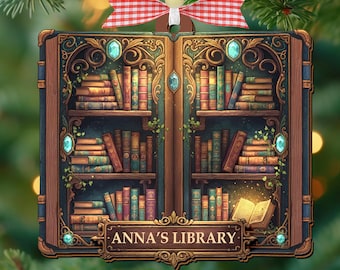 May include: A Christmas tree ornament shaped like an open book, featuring a detailed illustration of a library. The shelves are filled with colorful books, with the text "ANNA'S LIBRARY" at the bottom. The ornament is decorated with a red and white checkered bow.