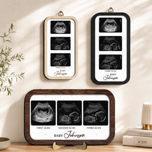 Könnte beinhalten: Drei rechteckige Rahmen mit Ultraschallbildern. Zwei vertikale Rahmen in hellem Holz und Schwarz enthalten jeweils drei Scans mit dem Text "THIRD SCAN" und "BABY Johnson". Ein horizontaler Rahmen aus dunklem Holz enthält drei Scans mit der Beschriftung "FIRST SCAN", "SECOND SCAN", "THIRD SCAN" und "BABY Johnson".
