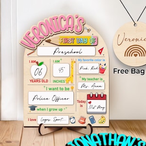 May include: Wooden first day of school sign with the name "Veronica's" in pink. The sign includes fields for age, height (114 cm), favourite colour, teacher's name, and future career. A matching bag tag is included.
