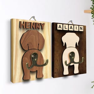 May include: Two wooden dog-shaped wall hooks. One is light wood with the name "HENRY" in raised letters. The other is dark wood with the name "ALAIN" spelled out in Scrabble tiles. Both have bronze-colored hooks.