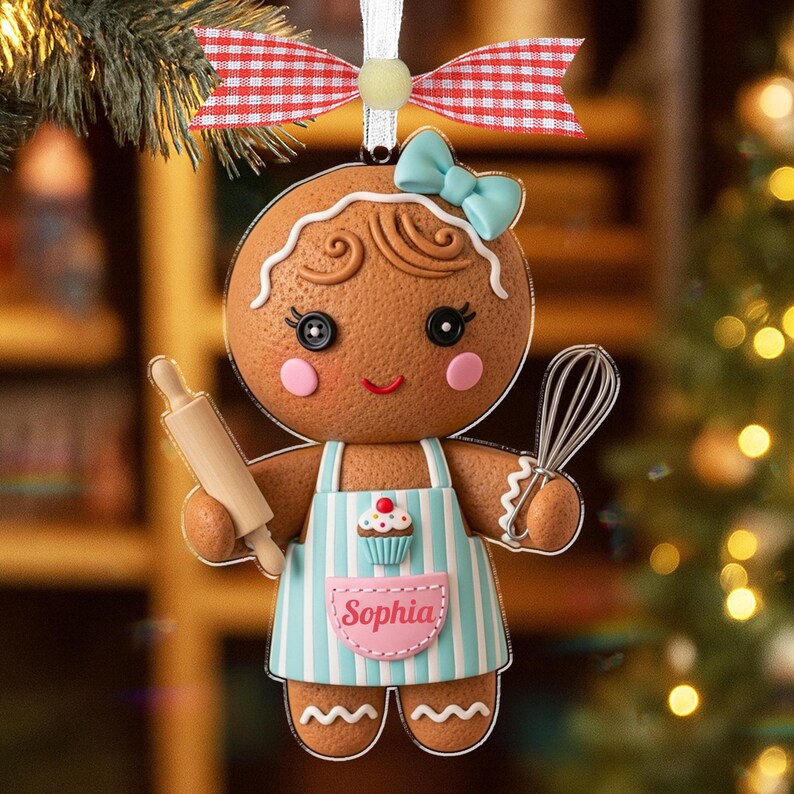 May include: A gingerbread-person Christmas ornament with a blue bow, apron, and rolling pin. The apron has blue stripes and a cupcake design. The ornament is personalized with the name "Sophia" and is decorated with a red and white checkered bow.